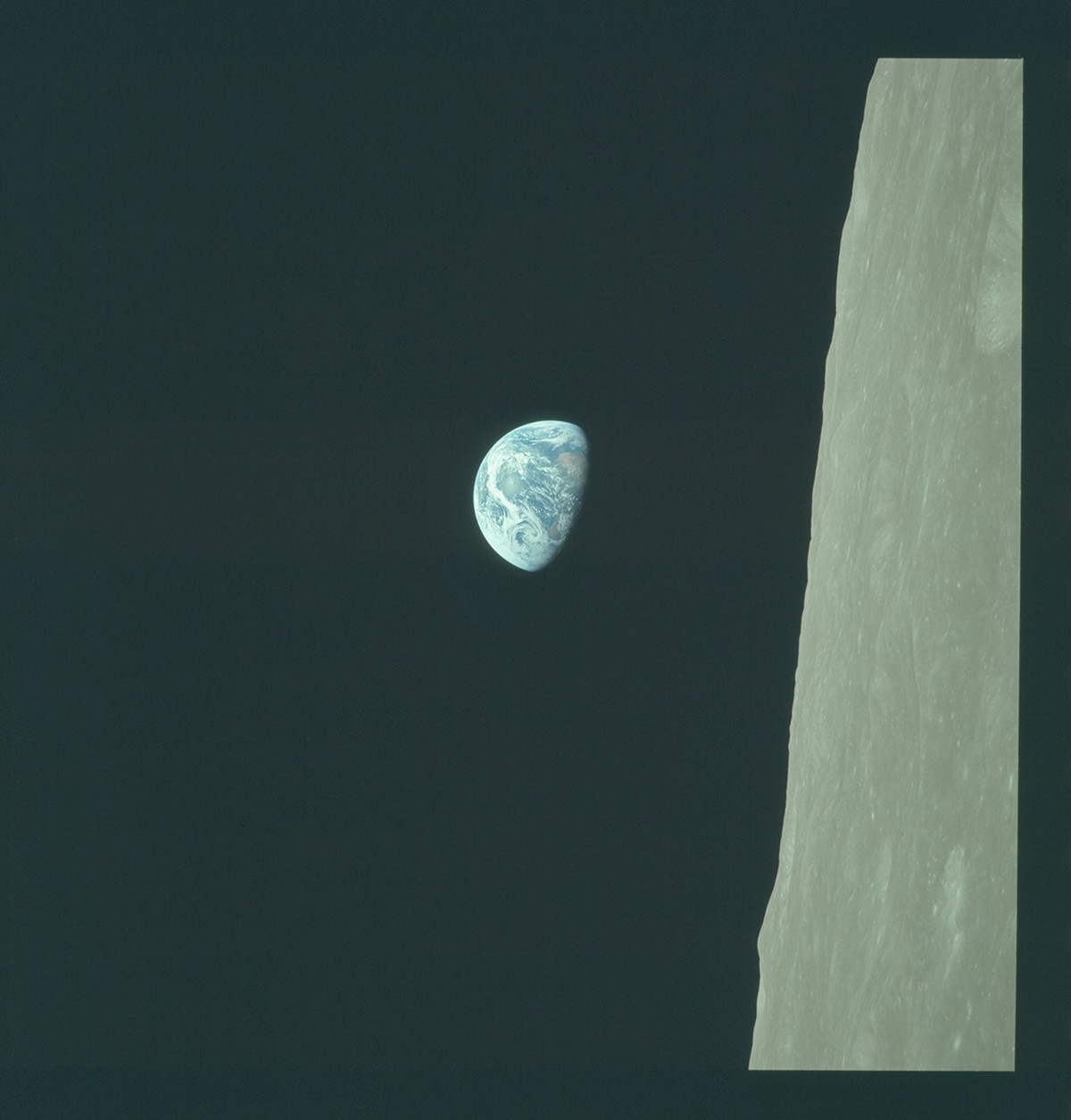 Blue-and-white Earth against dark space, beside pale lunar terrain running down the right side of the frame.